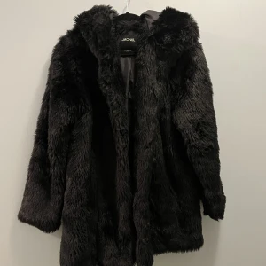Fuskpälsjacka - I använt skick men inga större skavanker. Har behövt sy fast knäppena några gånger (se bild 3). Det var en lång kappa från början men den är uppsydd av skräddare så inget som märks. Den har luva om det inte är 100% tydligt på bilderna!