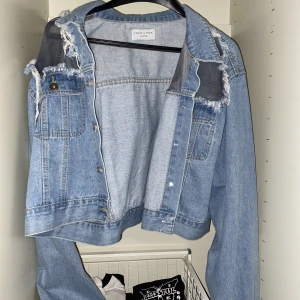 Blå jeansjacka  - Blå jeans jacka från liqour n poker! Den har öppna axlar, själv har jag aldrig använt den men den är från min syster och jag vet inte hur många gånger hon har haft den! Den är oxå kort vid midjan