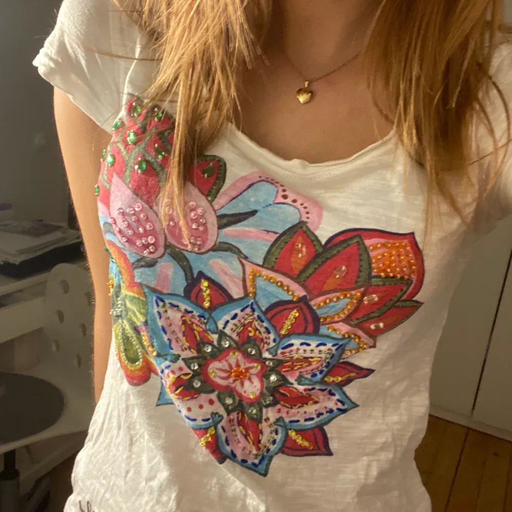 Vit T-shirt ifrån desigual med flerfärgad blomma med paljetter och stenar på🤍🤍Samt ett sött litet knyte där bak. T-shirts.