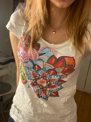 T-shirt  - Vit T-shirt ifrån desigual med flerfärgad blomma med paljetter och stenar på🤍🤍Samt ett sött litet knyte där bak