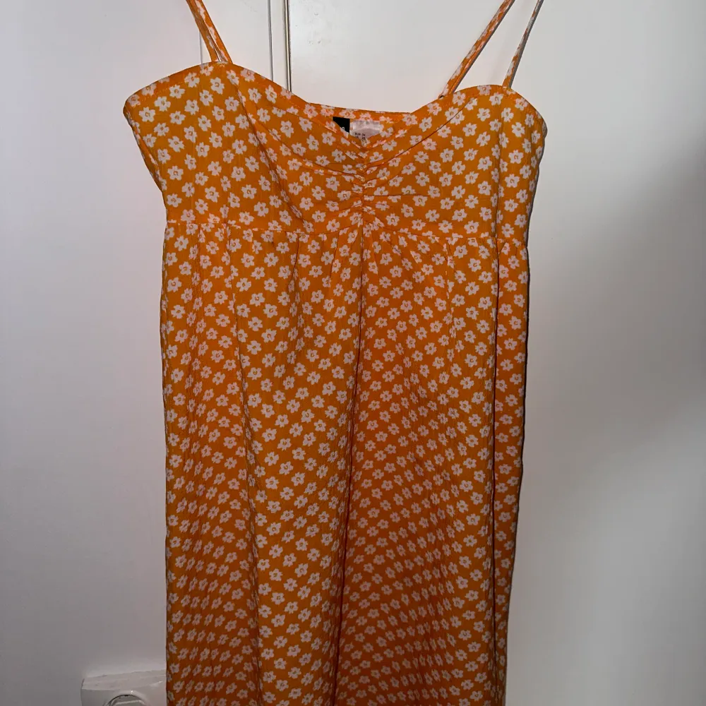Säljer denna super söta orangea klänning med vita blommor. Klänningen är i xs och den har nu blivit för kort för mig💞✨  Den kommer ifrån divided - HM. Dragkedja på sidan och ihopdraget mellan brösten👌🏼✨💞. Klänningar.