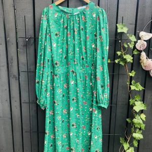 Snyggaste klargröna klänningen med blommönster!  - Så fin klänning från Ellos med ärtgrön botten och blommönster i rosa, gult, orange mm.  Material: polyester. Storlek: 48. Fina långa ballongärmar. Vid kjoldel. Så smickrande modell! Superfint skick!   