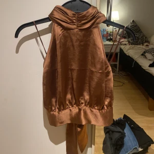 Festtopp - Snygg brun halterneck med öppen rygg från BikBok. Knäpps med tre knappar runt halsen, finns en extraknapp om någon lossnar. Sidorna knyts bakom ryggen, därav passar den flera storlekar.