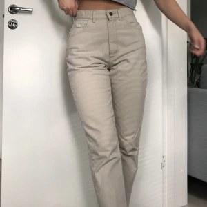 Beiga Lee jeans - Ljusa grå-beige jeans i tjockt material av bra kvalitet.  Köptes som 2nd hand med en liten fläck på  knät som knappt syns i vanligt bruk.    Sitter åt perfekt i midjan och har raka ben.   Tyvärr lite för små för mig men annars perfekta mom-jeans!