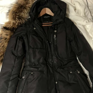 Hollies jacka  - En jätte fin svart hollies jacka, i väldigt bra skick. Har används men är fortfarande som ny. Den är tjock och jätte varm, skyddar mot flera - grader. Kommer med äkta päls, men man kan även köpa den utan pälsen 