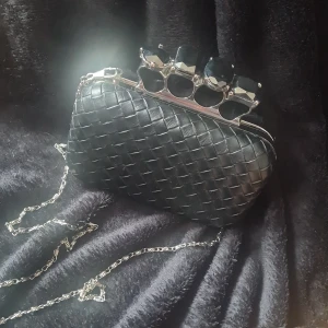 Handväska  - Mindre handväska i läderimitation. Axelledja och handtag som är ringar.