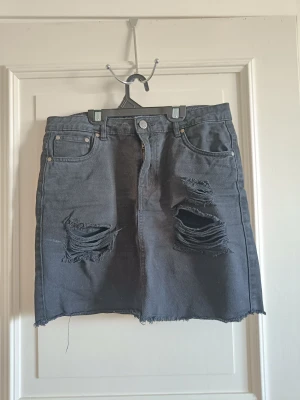 Jeanskjol, Nelly - Svart jeanskjol från Nelly med slitningar. Storlek 34/XS, för liten för mig som vanligtvis är en small så skulle säga att den är true to size. Endast använd fåtal gånger, fortfarande i fint skick.