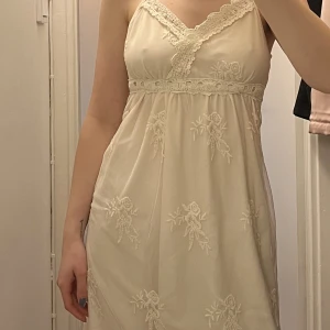 Sommarklänning  - Så söt krämvit sommarklänning med spets från Vila. Klänningen har ett band i spets som kan knytas antingen bak i ryggen eller viras ett varv runt och knytas framme. Endast använd ett fåtal gånger. Storlek S med justerbara axelband. 