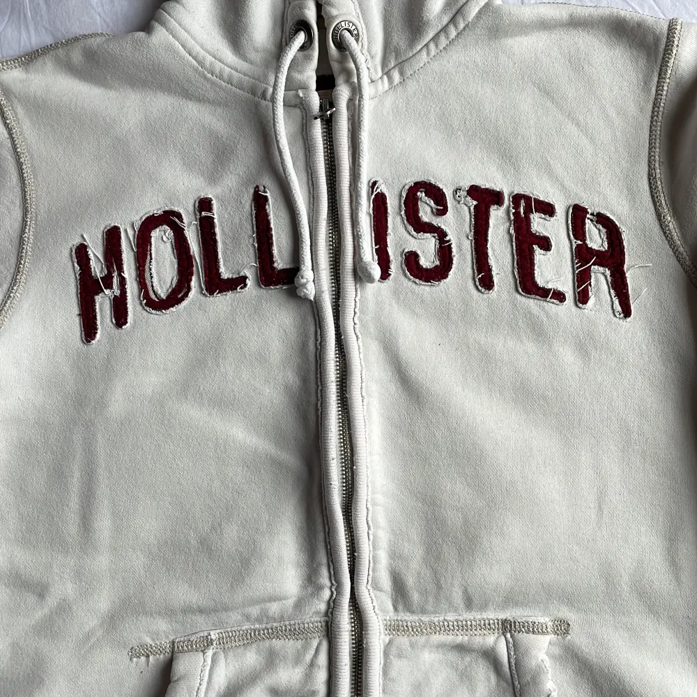 En vit Hollister zip-up tröja i utmärkt skick. Den är märkt som storlek S, men den kan bekvämt passa någon som normalt bär storlek M.. Hoodies.