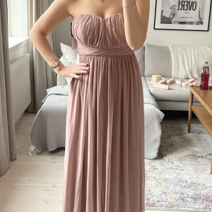 Balklänning NLY EVE - Balklänning från Nelly. Multi-tie funktion så den går att knyta på flera olika sätt. Puderrosa/dusty pink. Helt oanvänd med prislappar kvar. Nypris 899kr. Storlek 36 men skulle även säga att den passar 38. Perfekt till studentbal eller liknande!