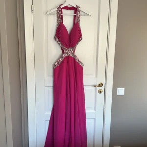 Balklänning  - Lång balklänning med cut-out vid midjan. Klänningen är i strl L och är helt oanvänd så därav i nyskick.