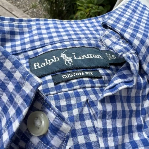 Rutig skjorta från Ralph Lauren - Klassisk blå-vit rutig skjorta. Sparsamt använd. Custom fit och storlek medium. Observera sista bilden där en mindre fläck finns (kan gå bort i tvätt?).  Se gärna mina övriga försäljningar för fler fynd 🙏