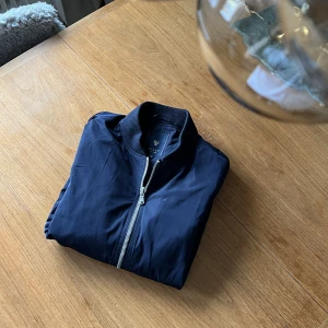 Stilig jacka (mörkblå) - Medium - En jacka i bomber-modell. Den upplevs stiligare än ”vanlig” bomberjacka då den är mer rak i modellen. Fickor finns både utanpå och insidan. I väldigt fint skick, ser ut som ny. Storlek 48 (medium).