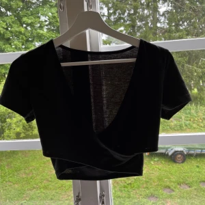 Topp - Svart kort topp med korsat tyg framtill. Som man ser på bilden är tyget lätt genomskinligt. Aldrig använd pga fel storlek.