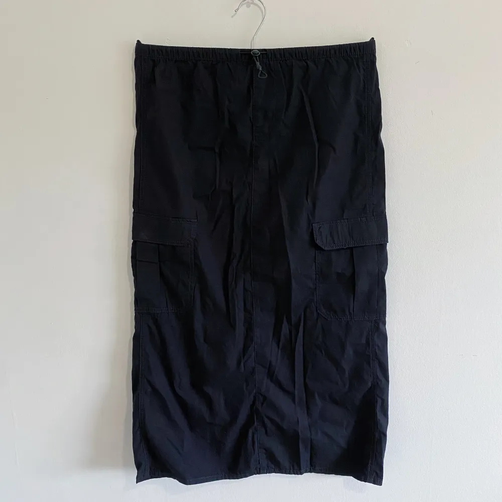 Oanvänd svart cargokjol från H&M. Dragsko i midjan men många fickor, slitt i bak. Längd: 28 cm.. Kjolar.