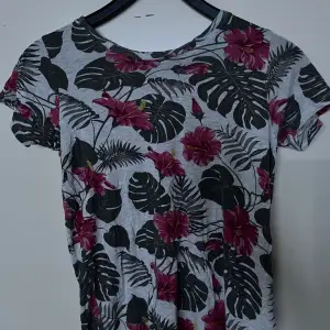 T-shirten är i väldigt bra skick. Det är en somrig T-shirt med rosa blommor och gröna blad på en grå-vit/ ljus grå bas. 