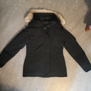 Canada Goose - MonteBello Parka (Small) - Varm dunjacka från Canada Goose med löstagbar äkta päls på luvan. Fyra framfickor med skönt fleecefoder samt en ficka på vänster ärm och två praktiska innerfickor. Stängs med kraftig dragkedja och knappar.  Knappt använd så mycket fint skick. Storlek: S