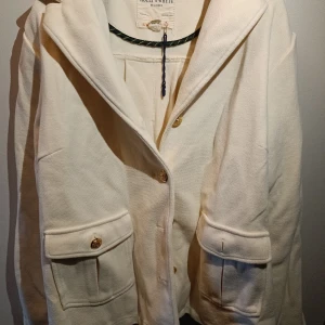 Vit kappa i storlek XL - En vit kappa med guldiga knappar från Holly and Whyte i storlek XL, helt oanvänd! 