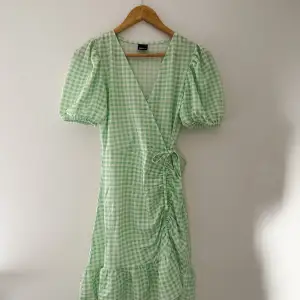 Superfin grön och vit rutig klänning från Gina Tricot som tyvärr aldrig kommit till användning, så är i helt nytt skick. Perfekt lätt klänning till sommaren och midsommar. Har en detalj på sidan av höften med knyten. Är i storlek XS