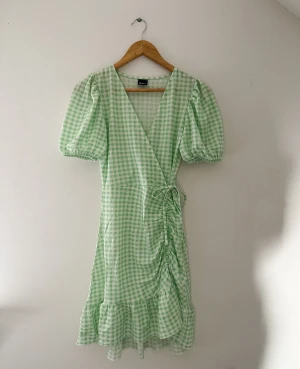 Klänning - Superfin grön och vit rutig klänning från Gina Tricot som tyvärr aldrig kommit till användning, så är i helt nytt skick. Perfekt lätt klänning till sommaren och midsommar. Har en detalj på sidan av höften med knyten. Är i storlek XS