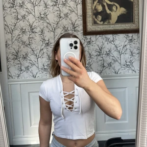 T-shirt med snörning - En vit T-shirt som är lite kroppad samt har en snörning vid bröstet. Från Nelly trend.