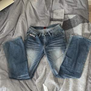 Snygga vintage jeans i 100% bomull. Super söt blomtag och röd detalj på baksidan. Ingen skada på fickor/ändan av jeansen. Slitet i färgen längst lår/knän. Tajta i övre lår. Low waist & utåtgående från knäna. Snyggt till en enkel tisha och smycken!