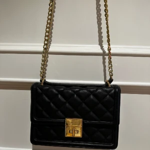 Quiltad väska från Aldo - Svart quiltad väska med lång guldkedja från Aldo. Fint skick.