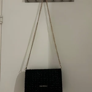 Valentino väska - jag säljer denna superfina väska från valentino, den ör svart och har en guld kedja. Med väskan får du en röd valentino påse. Jag har aldrig använt väskan eftersom den var inte i min smak  ! Den ör dock jöttebra om man vill få plats med mycket! priset änd