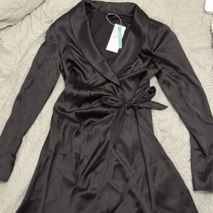 Blazer dress  - Snygg svart sidenklänning i kavaj/ omlott modell. Axelvaddar och snörning som man själv justerar. Oanvänd med tagg kvar. 