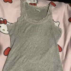 Grått spets linne - Säljer pga storlek! Y2k Aktigt Linne med spets ifrån Cubus som köptes för 3+ årsedan. Användes lite i början men vart sedan för liten. Sömmarna är hela det enda är väll att någon tråd sticker ut lite, men går och klippa bort :) !Katt finns i hemmet! 