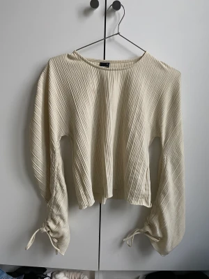 Blus Gina tricot  - Beige blus. Man kan dra åt vid armarna och göra en Knut eller låta de va som de är