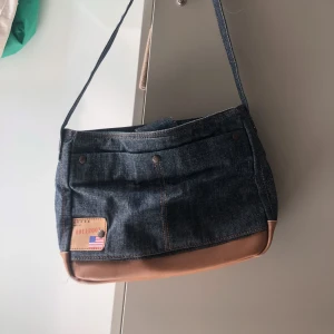 Handväska - Guess - Handväska från Guess i jeanstyg med bruna detaljer. Många fickor och utrymme! 
