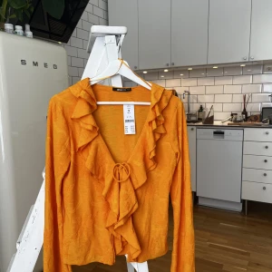 Orange topp  - Superfin orange topp med volanger! Aldrig använd med prislapp kvar så den är i fint skick. Köpt för 359kr