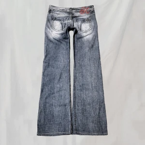 Lågmidjade jeans - Midja:79 innerben:79 Lågmidjade jeans med detaljerade bakfickor. Rött broderi och några små stjärnor med rhinstones. Stl w26. Uppsydda vilket kan ses som något ojämt, men skulle ej säga att det är något man tänker på när man bär de. Överlag fint skick !🤍