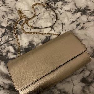 Guld glitter väska  - Jag säljer nu min gulliga väska då jag ej får någon användning av den längre. Den är köpt på H&M för ett tag sedan, använt på 3 bröllop. Inga tydliga skador eller repor. Den får plats med mycket innehåll. Köpt för 370kr säljer för 170kr