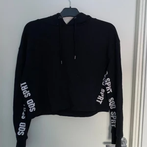 Svart kort hoodie - Svart kort hoodie med vit text på armarna, vet ej märket, bra skick men lite nopprig.