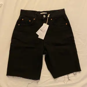 Jeansshorts utan stretch med en 90-talsinspirerad, rak passform. Shortsen är svarta och har en rå fåll längst ner. De har en längre längd. Köpt för 499 kr, säljes för 160 kr  Färg: black Mått: Innerbenssömmen är 23,5 cm i storlek M Modellen bär storlek 36