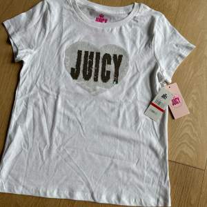 Vit Juicy t-shirt - aldrig använd med prislappen på. Vändbar paljett text ’Juicy’ som ändrar färg. Köpt i USA ($26). Vi köpte flera färger och av någon anledning blev den vita aldrig använd. 