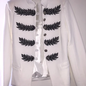 Blazer jacka/kofta - Vit blazer med snygga mörkgrå detaljer och silvriga knappar. Lätt vadderade axlar. Inga defekter. Onesize men passar S-M