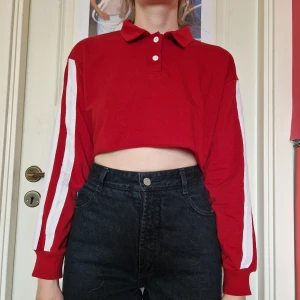 Croppad tröja - Croppad röd sweater med krage och 2 vita ränder längs armarna. Tyget är åt det tunnare hållet.  Står ingen storlek men skulle säga att den är XS–S.