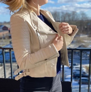 Vit skinnjacka - Somrig vit skinnjacka i begagnat skick. Lätt gulnad vid sömmarna i fodret på insidan. Allt är dock helt.  Dragkedjor och metalldetaljer i silver. Märke Voyelles, storlek 42.