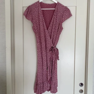 Söt omlottklänning - Jättesöt omlottklänning i rosa med vita blommor och kvistar. Storlek är onesize.  Aldrig använd, endast provad. Djur- och rökfritt hem.