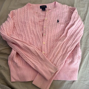 Rosa stickad kofta från Polo Ralph Lauren - Säljer en superfin rosa stickad kofta från Polo Ralph Lauren. Den har ett klassiskt flätmönster och knappar framtill. Perfekt för både vår och höst! 💖