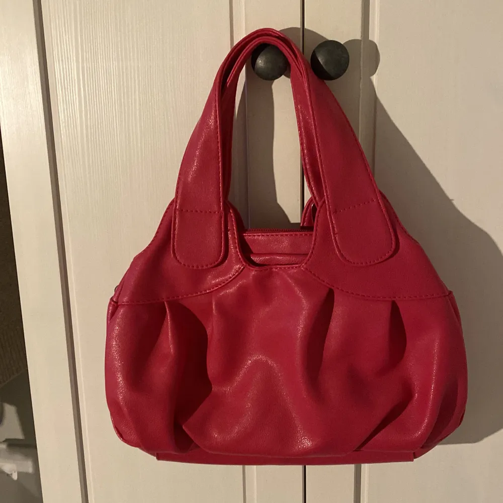 Säljer en snygg röd handväska från Sunnyshop. Väskan har en cool design med silverdetaljer och två rejäla handtag. Den är rymlig med flera fack inuti, perfekt för att hålla ordning på dina grejer. Väskan är i syntetmaterial och passar perfekt för både vardag och fest! den är lite mer åt rosa än röd men är en bra blandning därimellan!. Laukut & Käsilaukut.