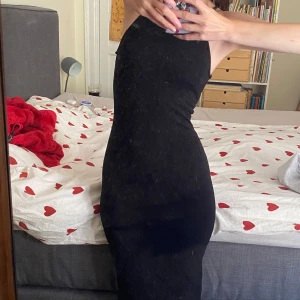 Svart tight klänning med slits - Säljer en elegant svart klänning som är perfekt för fest. Den är tight och smickrande med en stilren design. Klänningen har en slits baktill som ger en extra touch av stil. Den är ärmlös och har en hög halsringning, vilket gör den både modern och klassisk.