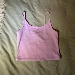 Lila ribbad linne - Säljer en superfin lila ribbad linne med smala axelband. Perfekt för sommardagar eller som ett lager under en tröja. Den är i bra skick och väldigt bekväm att ha på sig.