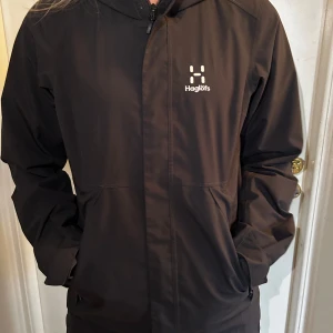 Svart vindjacka från Haglöfs - Säljer en svart vindjacka från Haglöfs. Den har en dragkedja framtill och är långärmad. Perfekt för blåsiga dagar och passar bra till både vardag och friluftsliv. Jackan är i bra väldigt bra skick och har inga som helst deffekter!