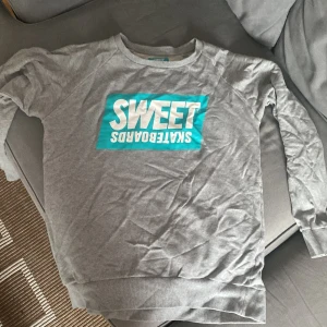 Grå sweatshirt från Sweet Skateboards - Säljer en grå sweatshirt från Sweet Skateboards med ett stort turkost och vitt tryck på framsidan. Tröjan har långa ärmar och en avslappnad passform, perfekt för en skön och stilren look.