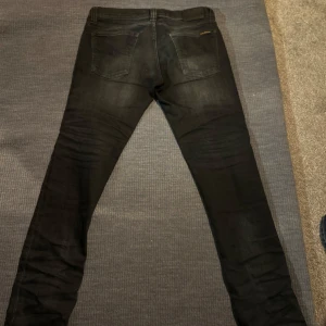 Svarta jeans från Nudie Jeans - Snygga svarta jeans från Nudie Jeans med en tight passform. De har klassisk femficksdesign och knappar i silverfärg. Perfekta för en stilren look. Skicket är 7/10 och finns tecken på användning. Ifall du har några frågor så är det bara att höra av sig! W29 L33