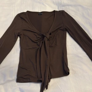 Brun långärmad topp med knyt - Snygg brun topp från Gina  med långa ärmar och en stilren knytning framtill. Perfekt för en chic och avslappnad look.